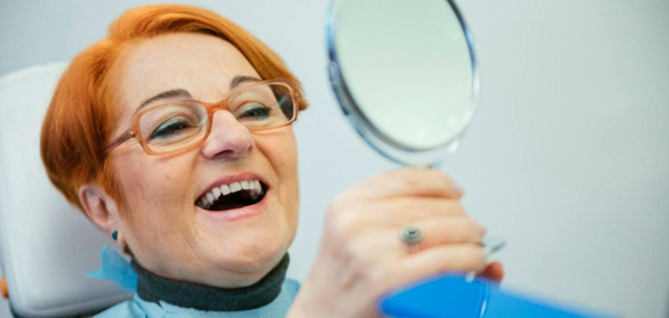 happy older woman looking in the mirror at the dentist’s office 