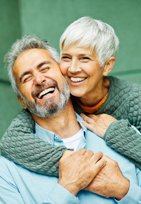 smiling couple hugging with a green background 