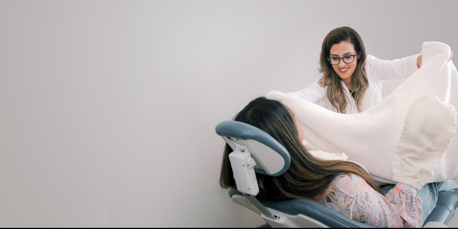 Doctor Tehrani placing a white blanket over a dental patient