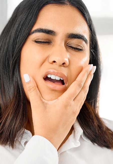 Woman in white shirt closing eyes in pain with hand pressed to jaw