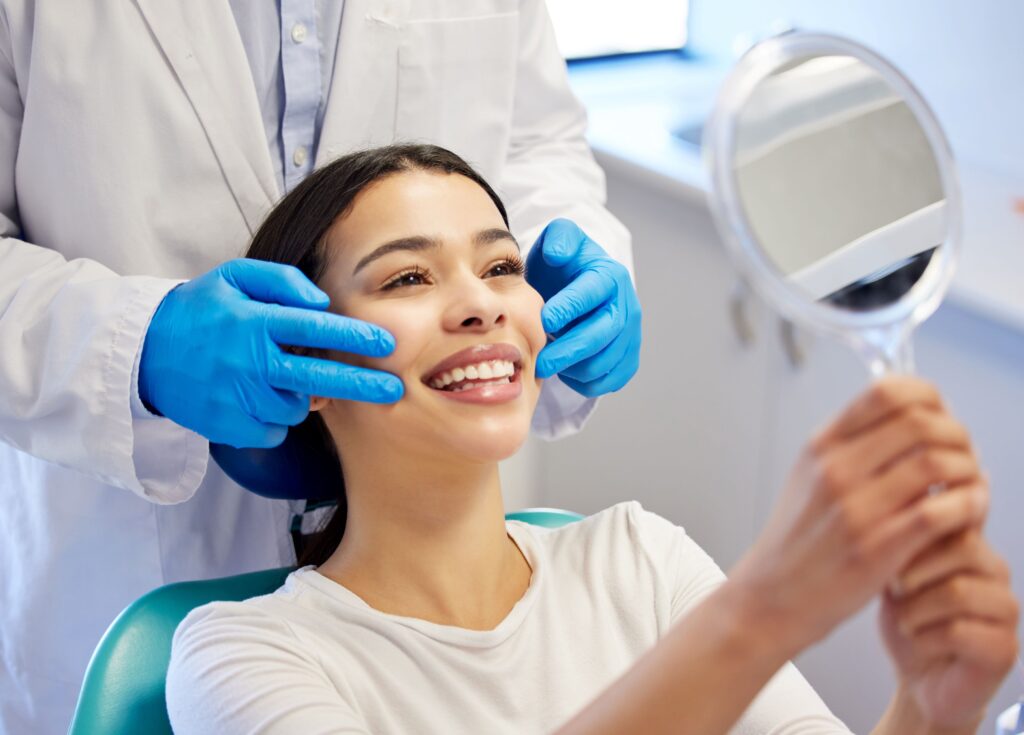 Woman in dental chair smiling with dentist in blue gloves touching her cheeks